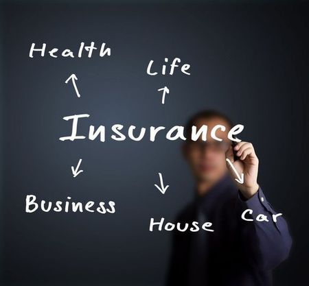 Person writing insurance-related words: Health, Life, Business, House, and Car, on a dark background.