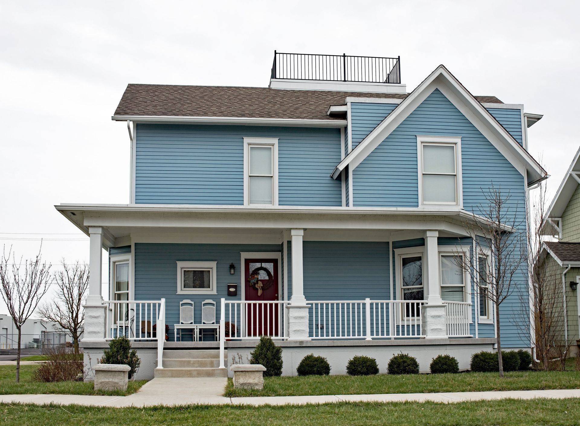 Blue two-story house with porch, white railings, and rooftop deck, set on green lawn.