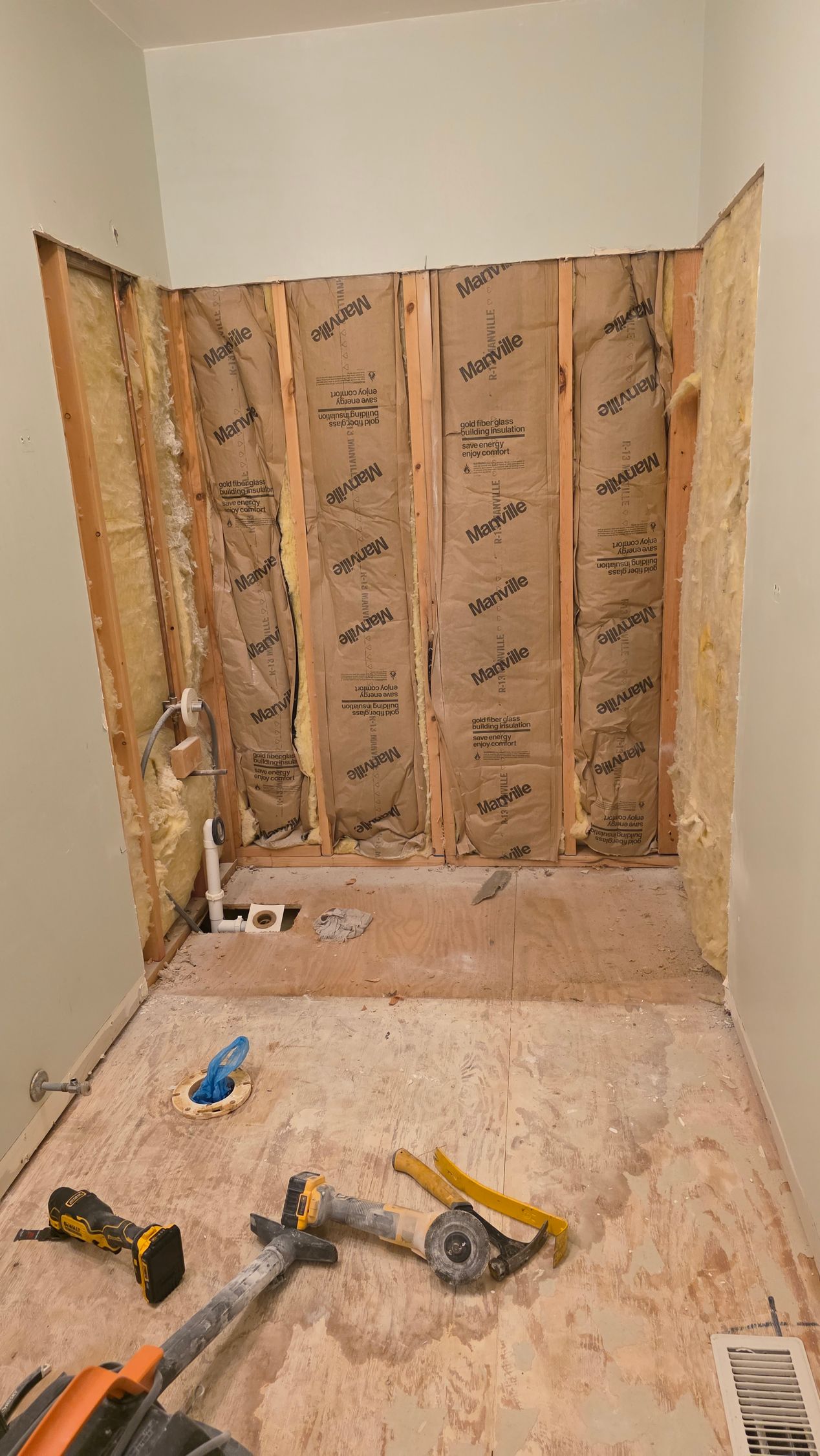 Bathroom renovation in progress; exposed studs, plumbing, and tools on wood subfloor. Walls are unpainted.