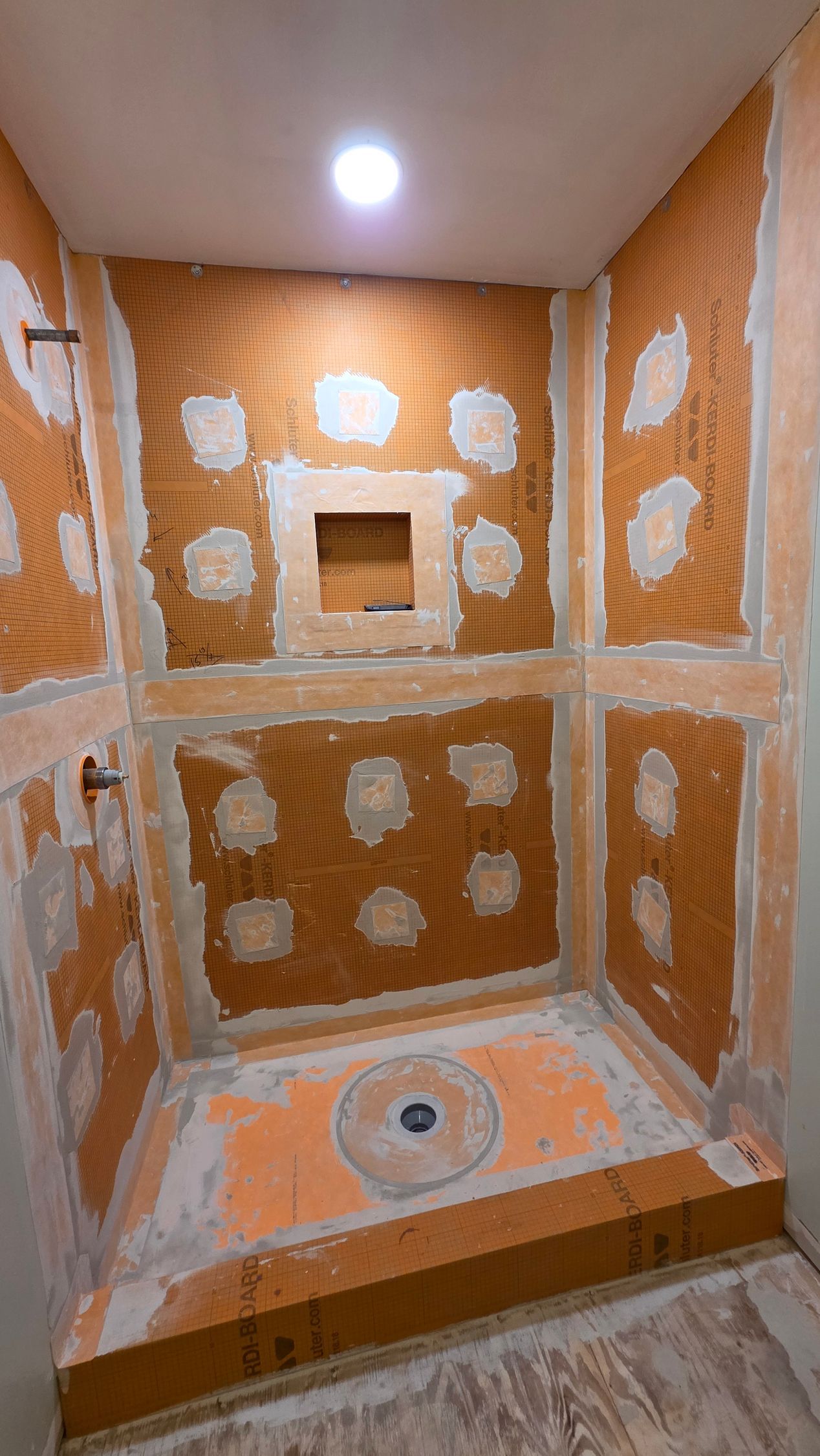 Shower stall under construction, orange mesh over cement walls. Orange and gray cement shower base with drain.