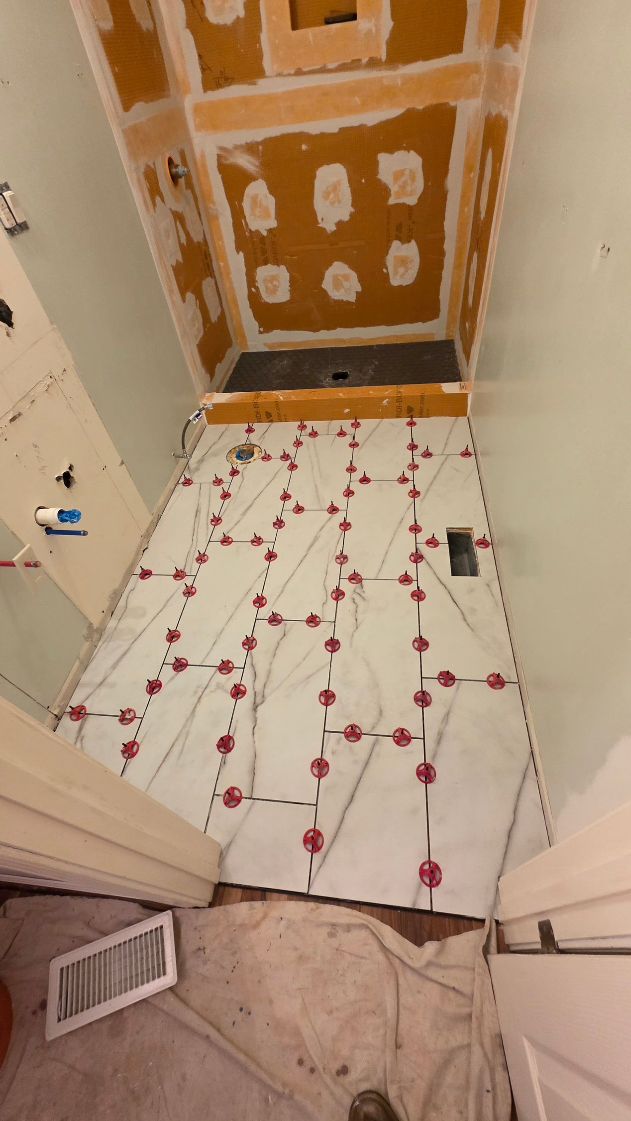 Bathroom floor tiling in progress, showing tiles with leveling system and ceiling partially tiled.