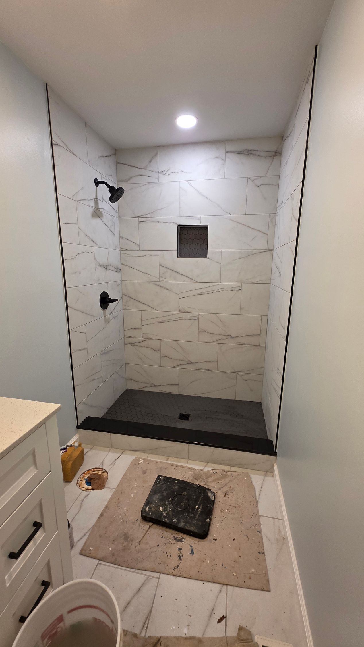 Bathroom shower under construction with white marble tile, black fixtures, and black shower floor.