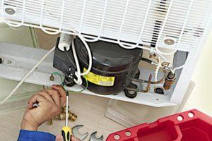 A man is fixing a refrigerator with a screwdriver.