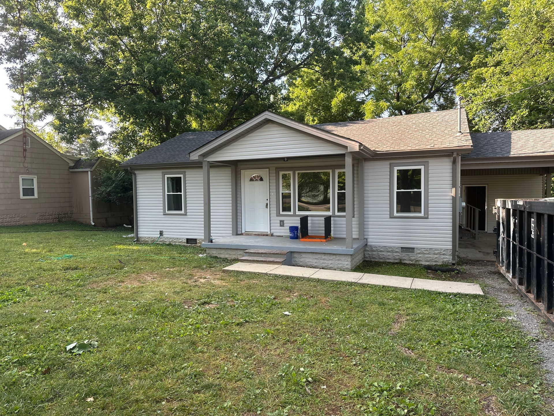 A small white house with a porch and a lot of grass in front of it.