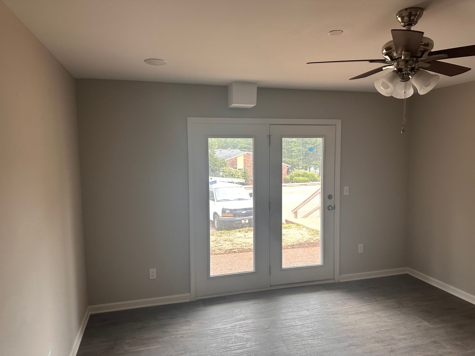 An empty room with a ceiling fan and sliding glass doors.