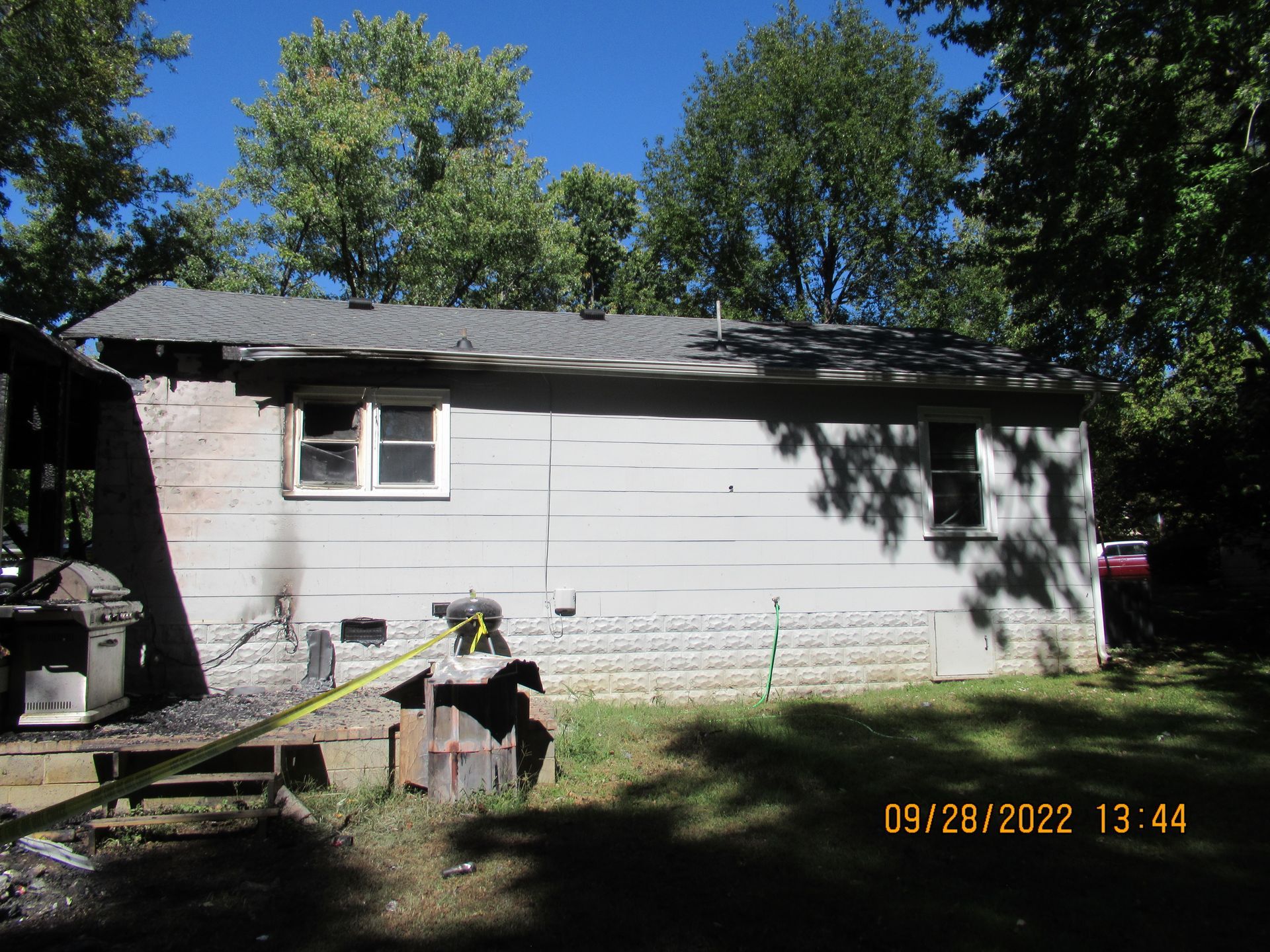 A white house with a gray roof is surrounded by trees on a sunny day.
