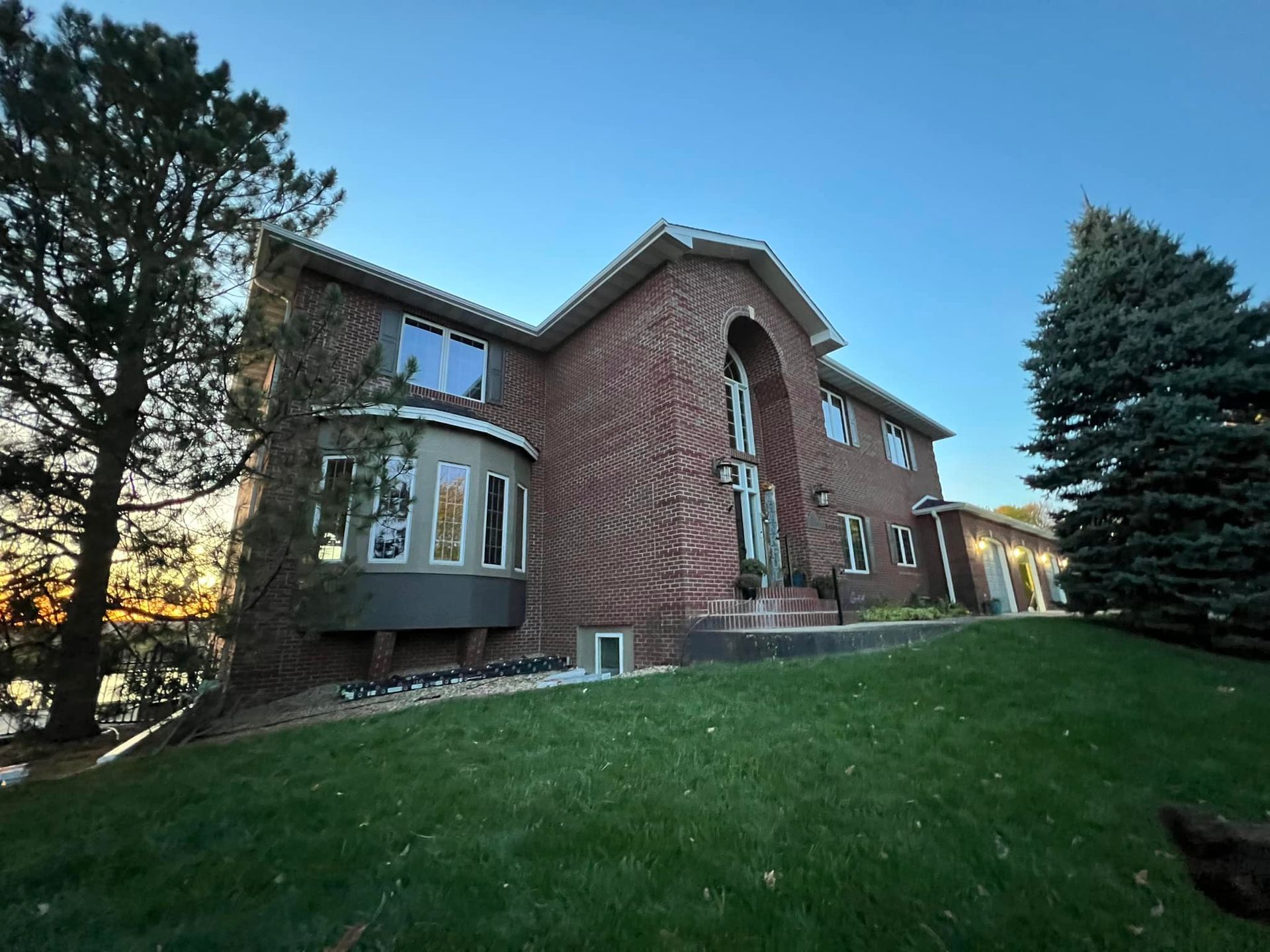 Brick two-story house with bay window and arched entry on a green lawn, under a blue sky.