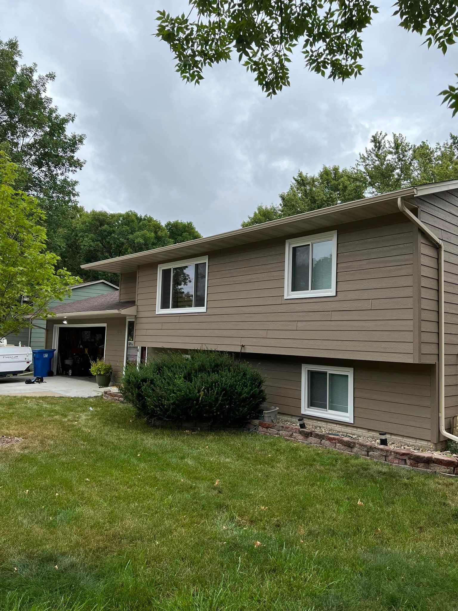 Two-story house with brown siding, white-framed windows, and green lawn. Overcast sky.