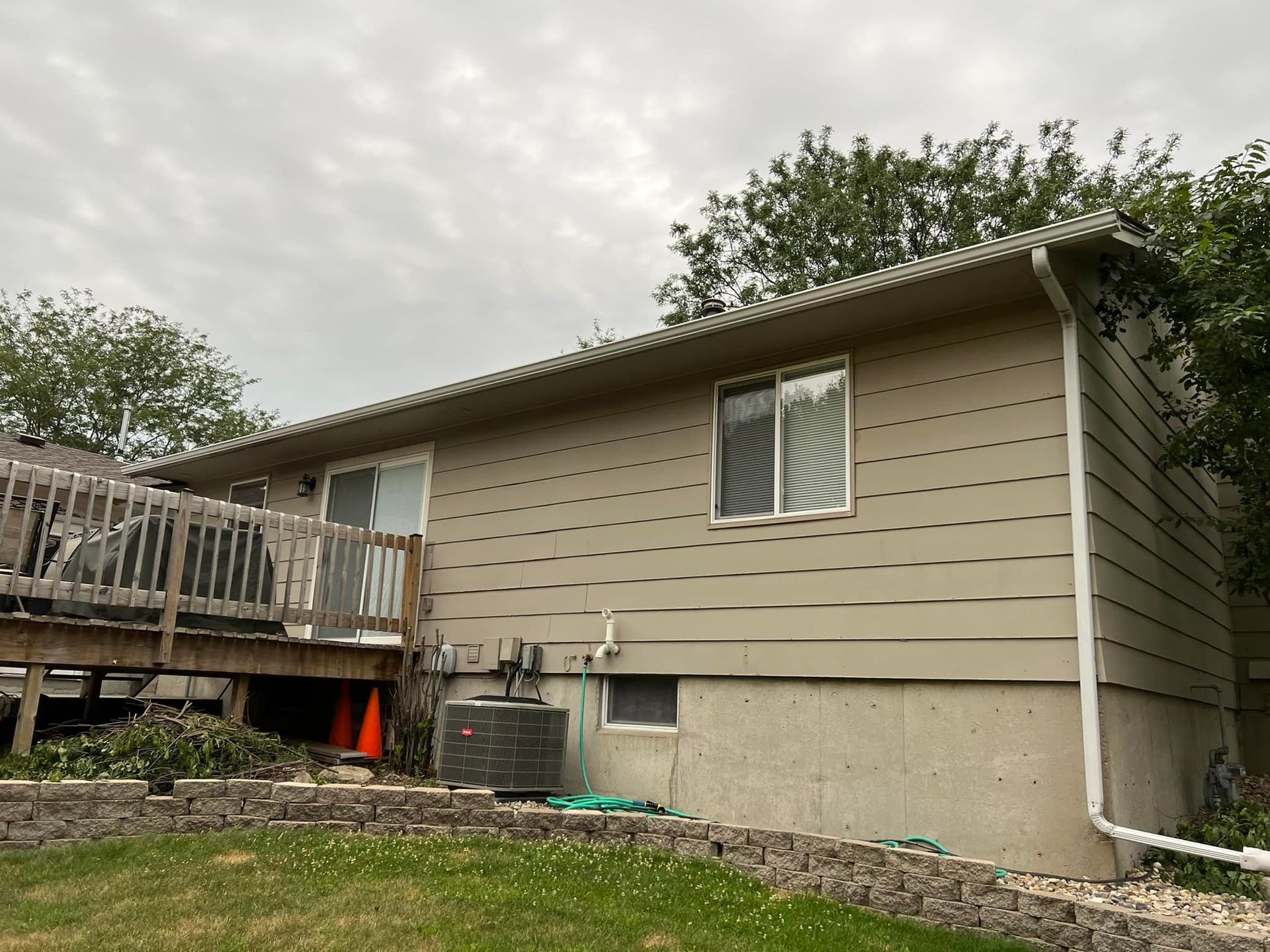 Tan-sided house with a deck and a cloudy sky. A window and sliding glass door are visible.