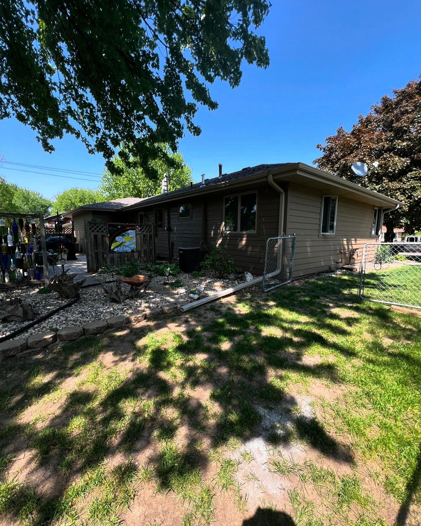 A one-story brown brick house with a green lawn and trees under a blue sky.