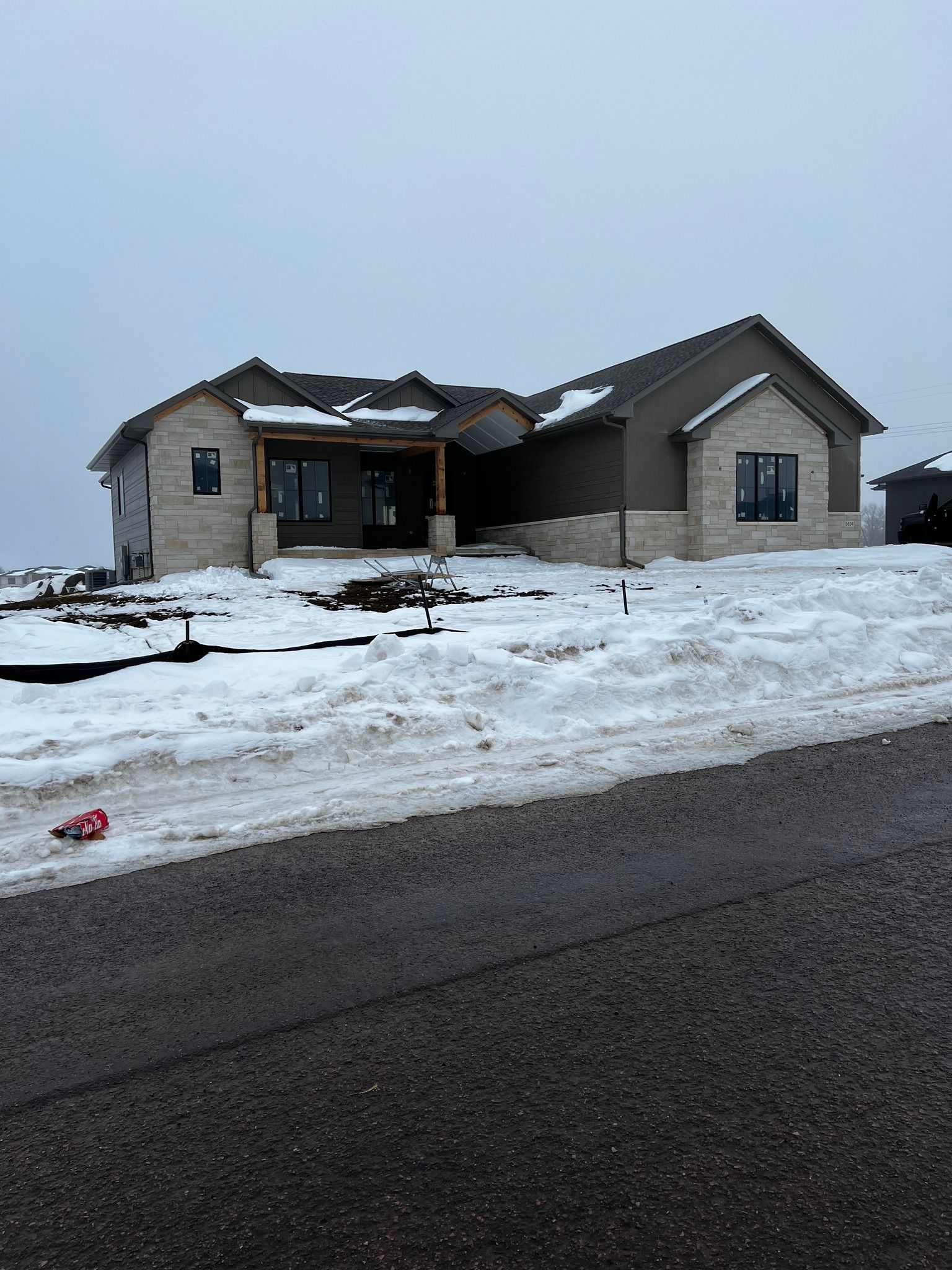 House under construction, beige brick and stucco, snow-covered ground, overcast sky.