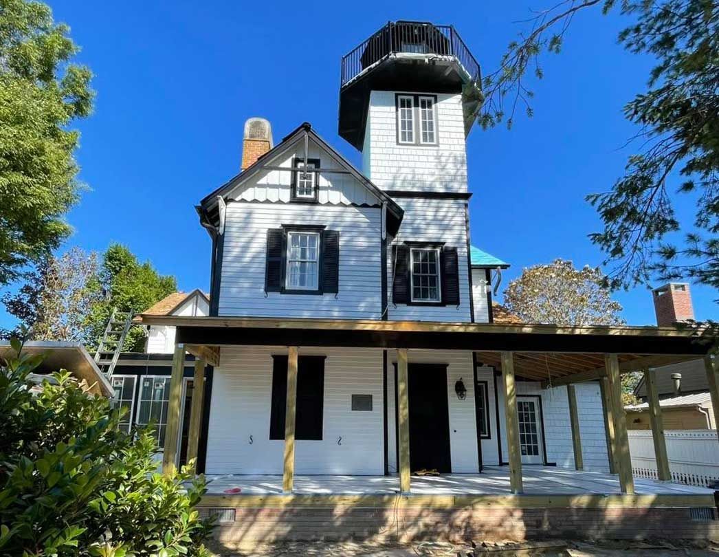 Old white Victorian-style house with a tower and wraparound porch under a clear blue sky