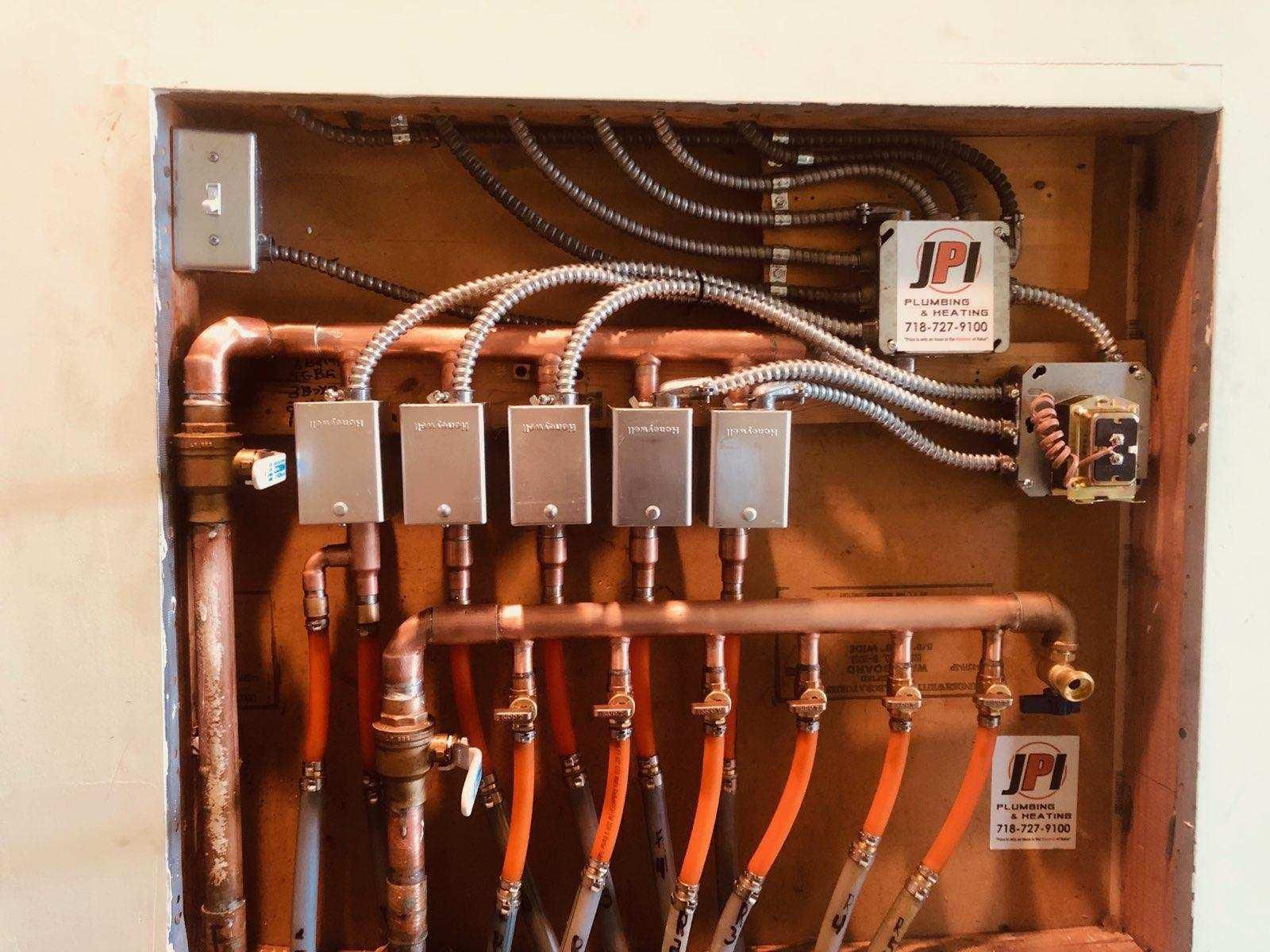 Electrical and plumbing panel with copper pipes, wiring, and labeled boxes mounted in a wooden recess.