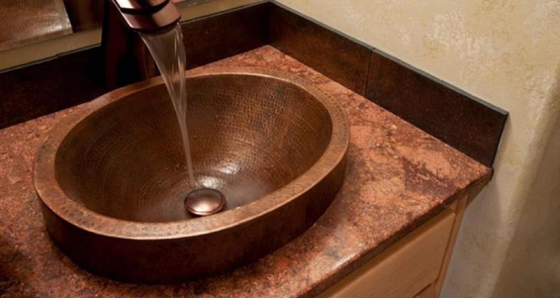 Copper sink with water flowing, set on a reddish-brown countertop.