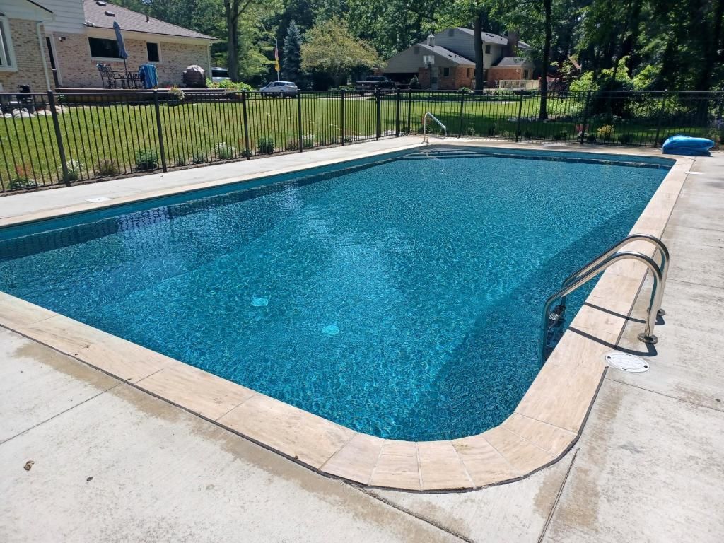 A large swimming pool with a fence around it and a house in the background.