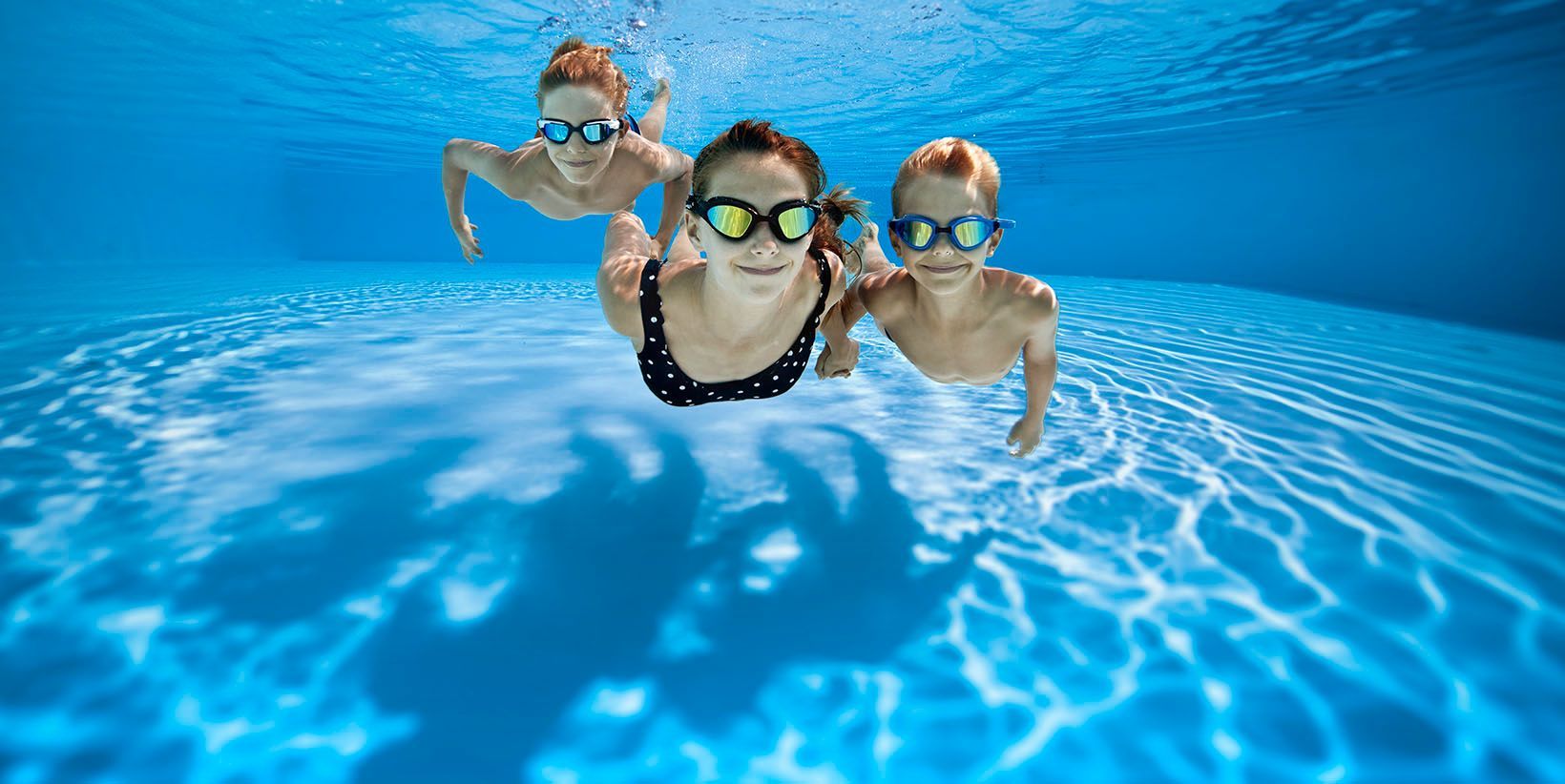 A woman and two children are swimming underwater in a swimming pool