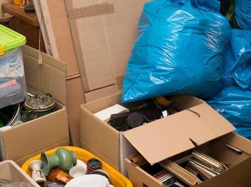 A pile of cardboard boxes filled with various items and a blue trash bag.