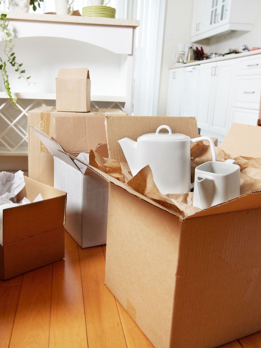 Cardboard boxes packed with items, including a teapot, in a room with wooden floors, preparing for a move