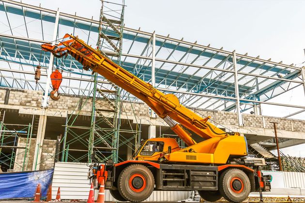 Orange crane lifting materials at a construction site with a steel-framed building in the background
