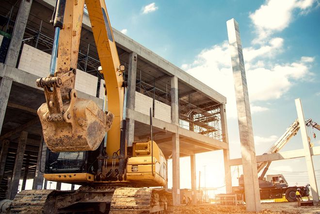 Construction site with excavator lifting debris beside a partially built concrete structure at sunset