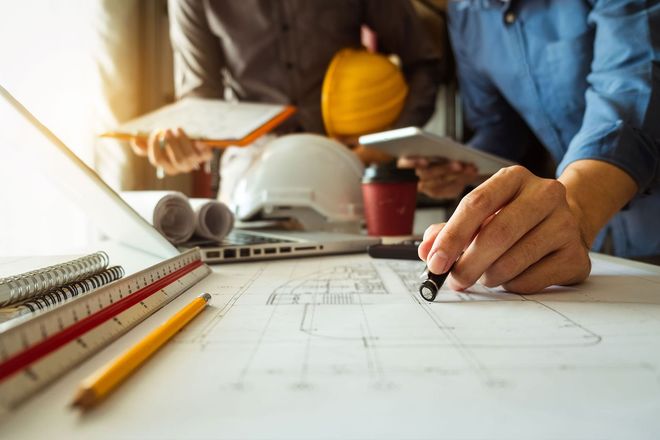 Architect drafting plans at a worktable with helmet, ruler, and pencil in a construction office