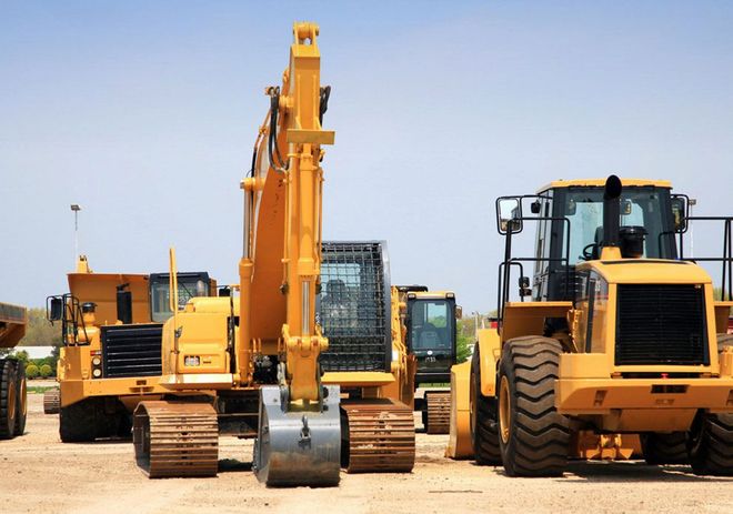 Yellow excavators and heavy construction vehicles lined up on a dirt lot under a clear sky.