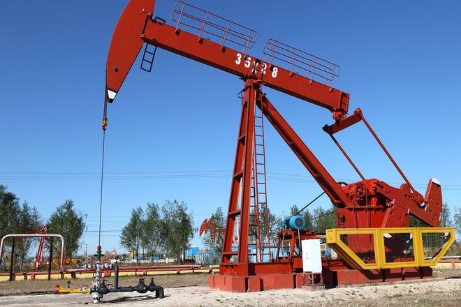 Red oil pumpjack in a field under a clear blue sky