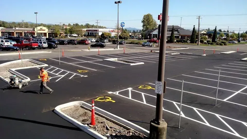 Parking lot with painted lines and a person walking; commercial buildings in the background.