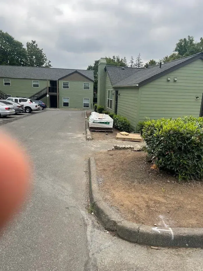 Apartment complex with green buildings, asphalt lot, parked cars, and cloudy sky.
