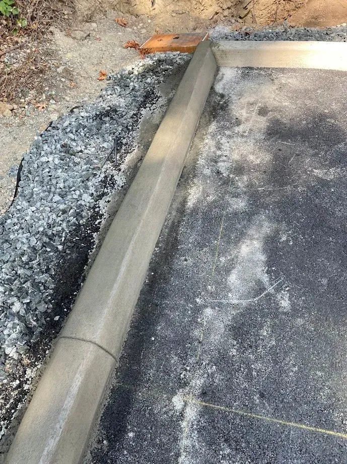 Newly poured concrete curb edging a dark asphalt surface with gravel nearby.