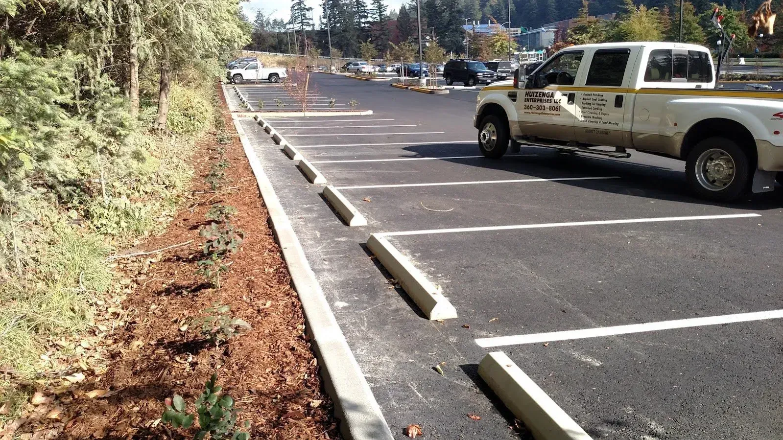 Parking lot with a white pickup truck, concrete parking stops, and a landscaped border.