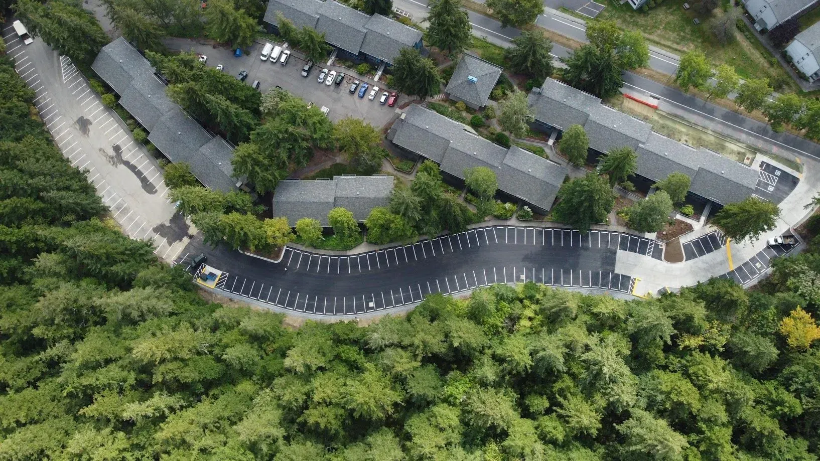 Aerial view of apartment complex with parking amidst lush green trees.