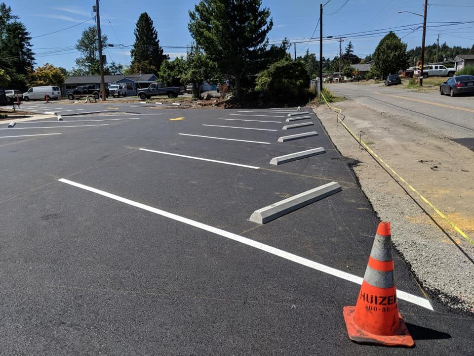 Newly paved parking lot with painted white lines, concrete parking stops, and an orange traffic cone.