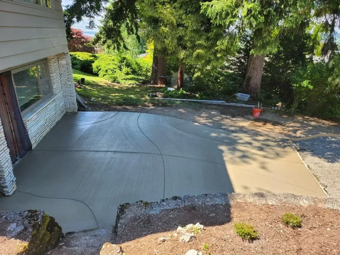 Freshly poured concrete patio next to a house with trees in the background.