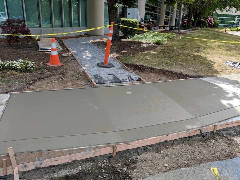 Freshly poured concrete sidewalk section, with wooden forms, and orange safety cones.