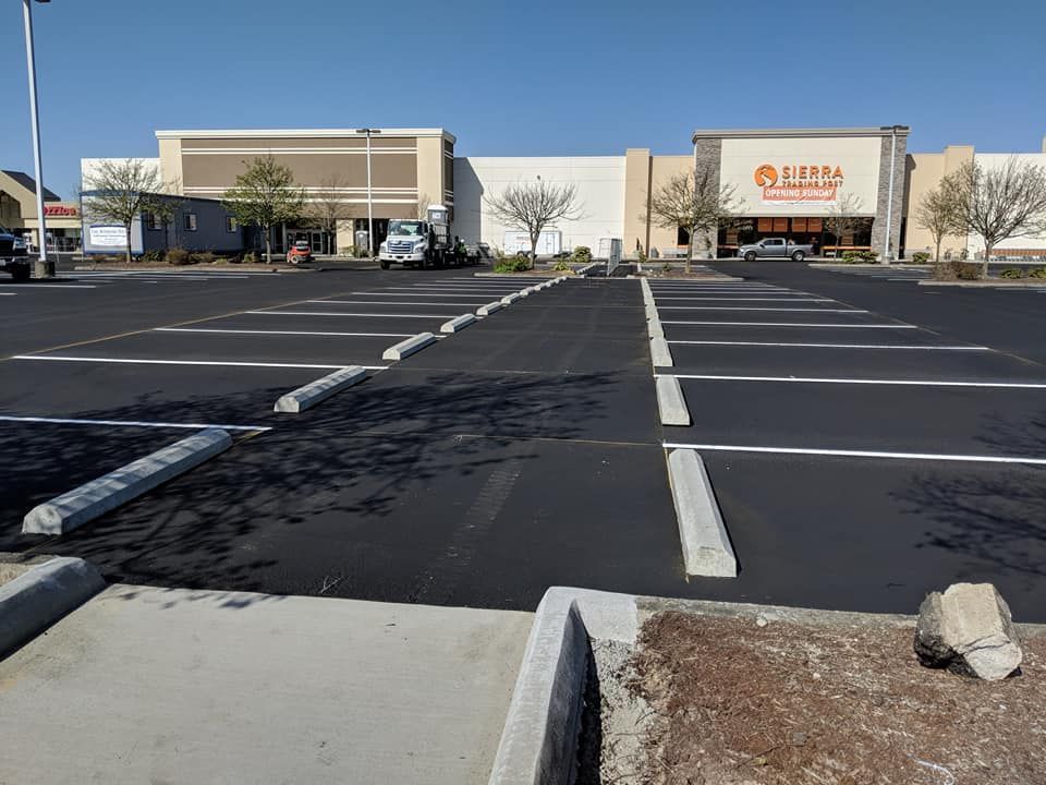 Black asphalt parking lot in front of a Sierra store with empty parking spaces and concrete barriers.