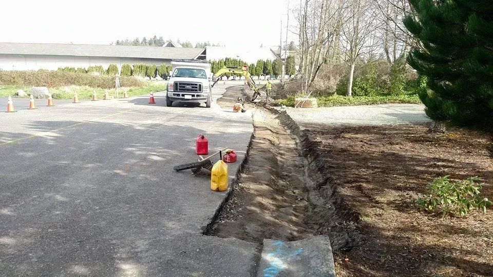 Road work in progress. Asphalt road with trench dug along the side. Truck, tools, and cones are visible.
