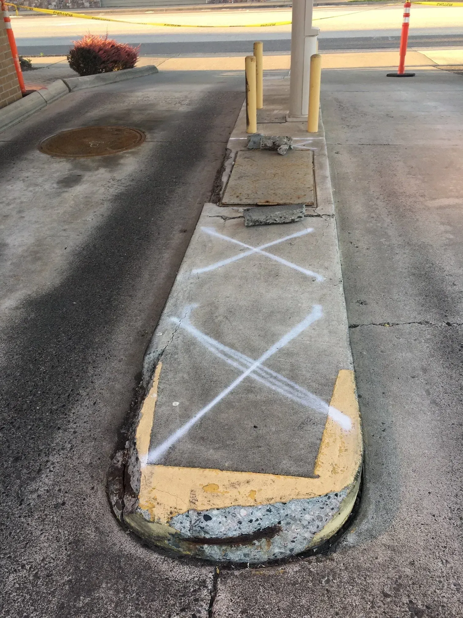 Concrete curb with white X markings, likely indicating repair needs, next to a gas station.
