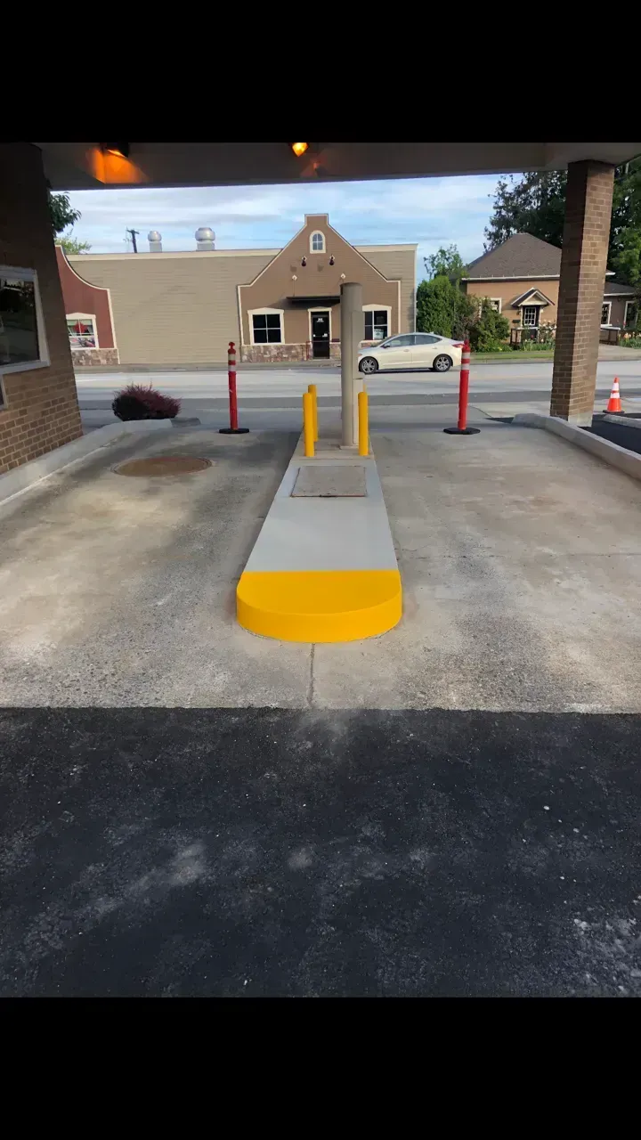 Drive-up bank teller lane with yellow and gray concrete divider, red poles, and building in the background.