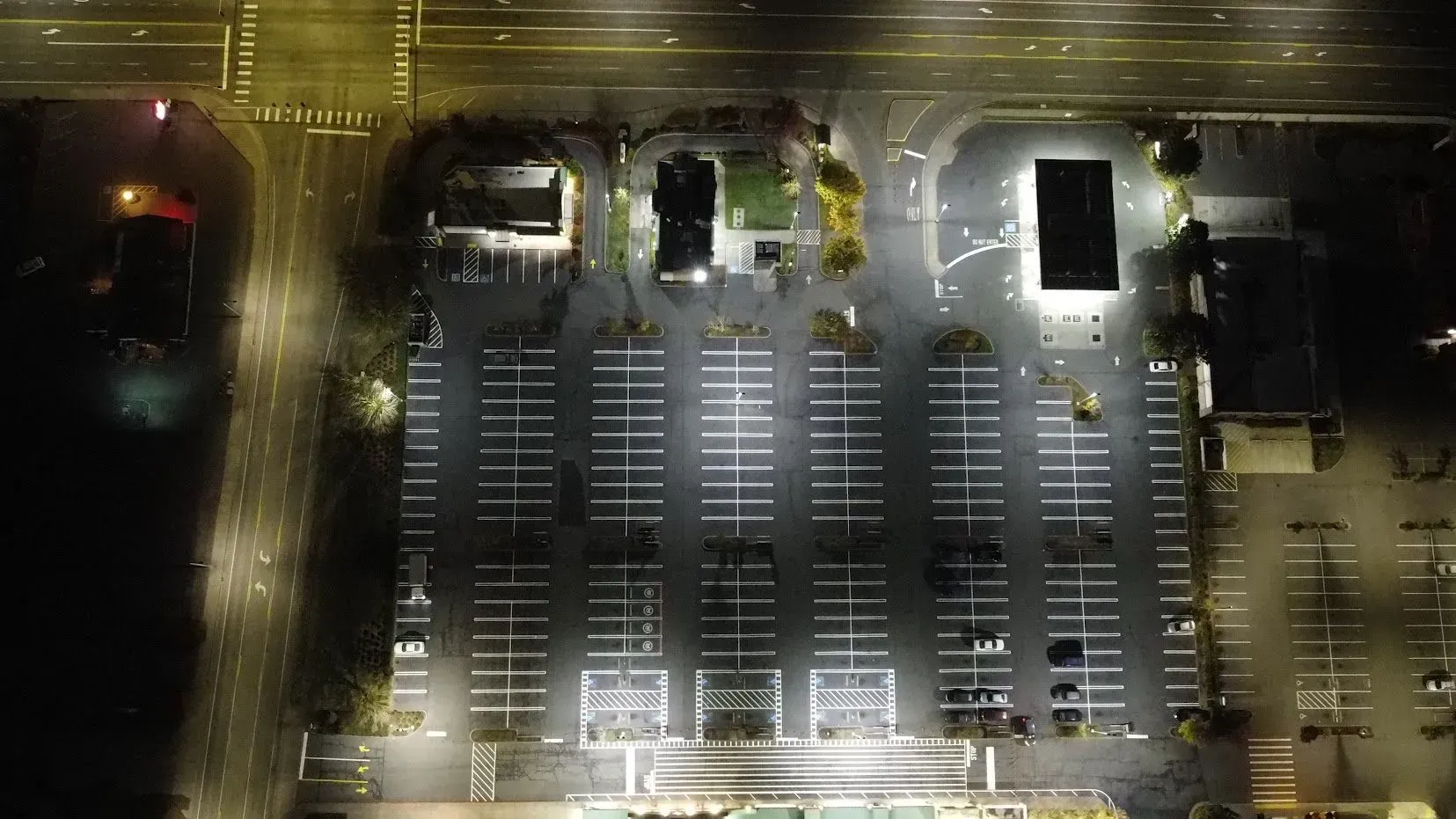 Aerial nighttime view of an empty parking lot, illuminated by streetlights and building lights.