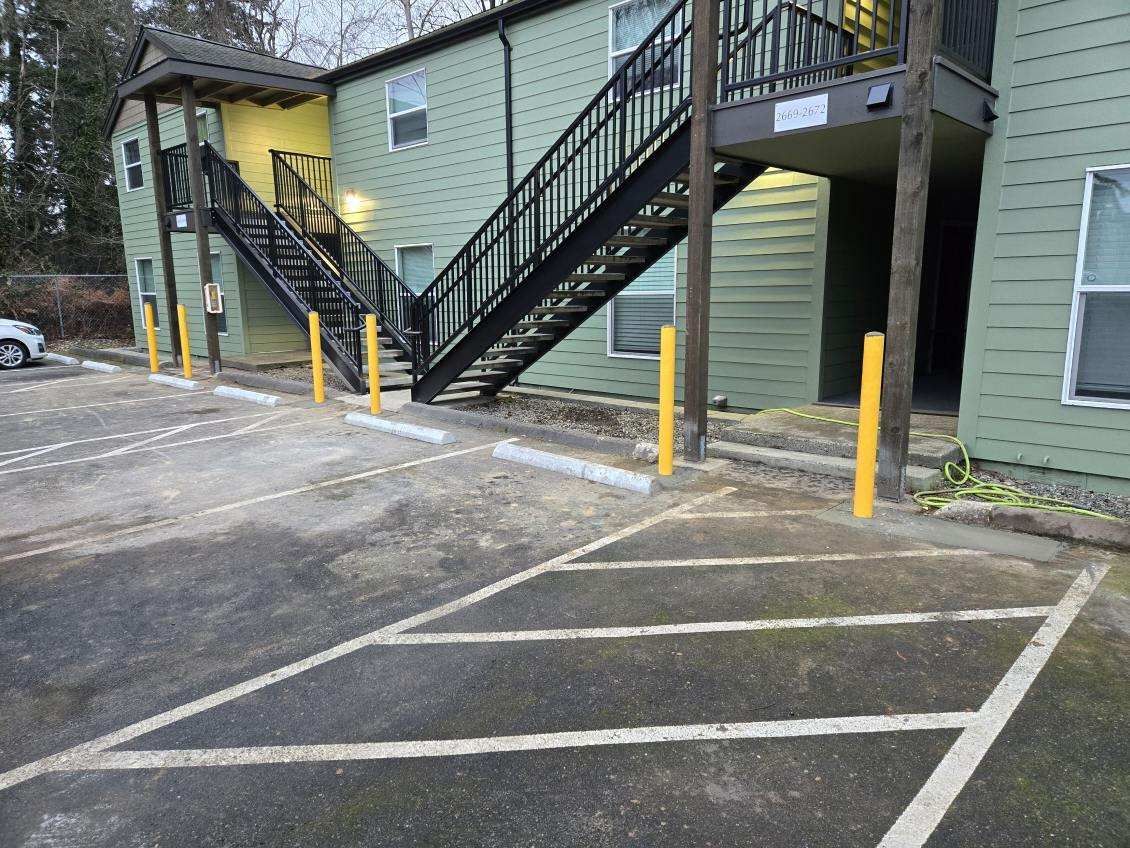 Exterior of an apartment building with parking spaces and stairwell, green siding and black stairs.