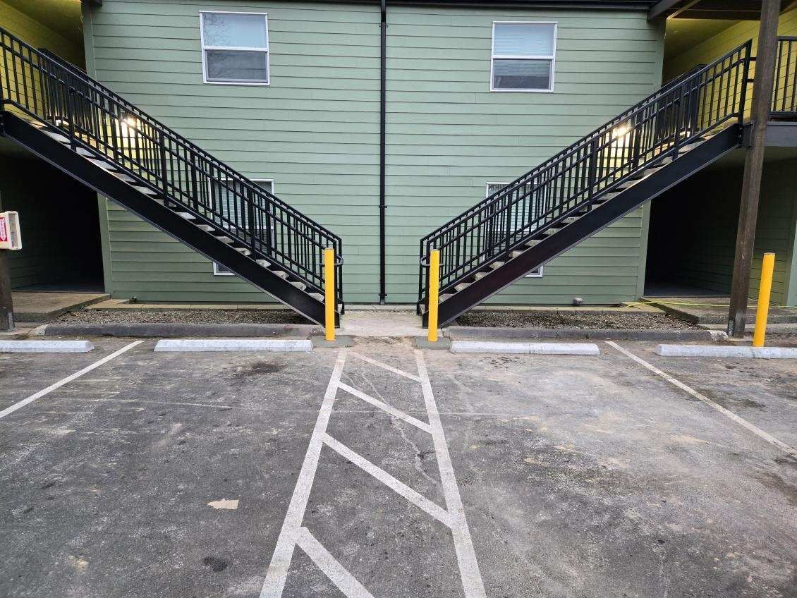 Black staircases on green building with parking space in front.