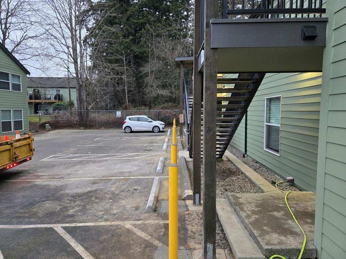 Parking lot with a white car, stairs, and a green building with windows.