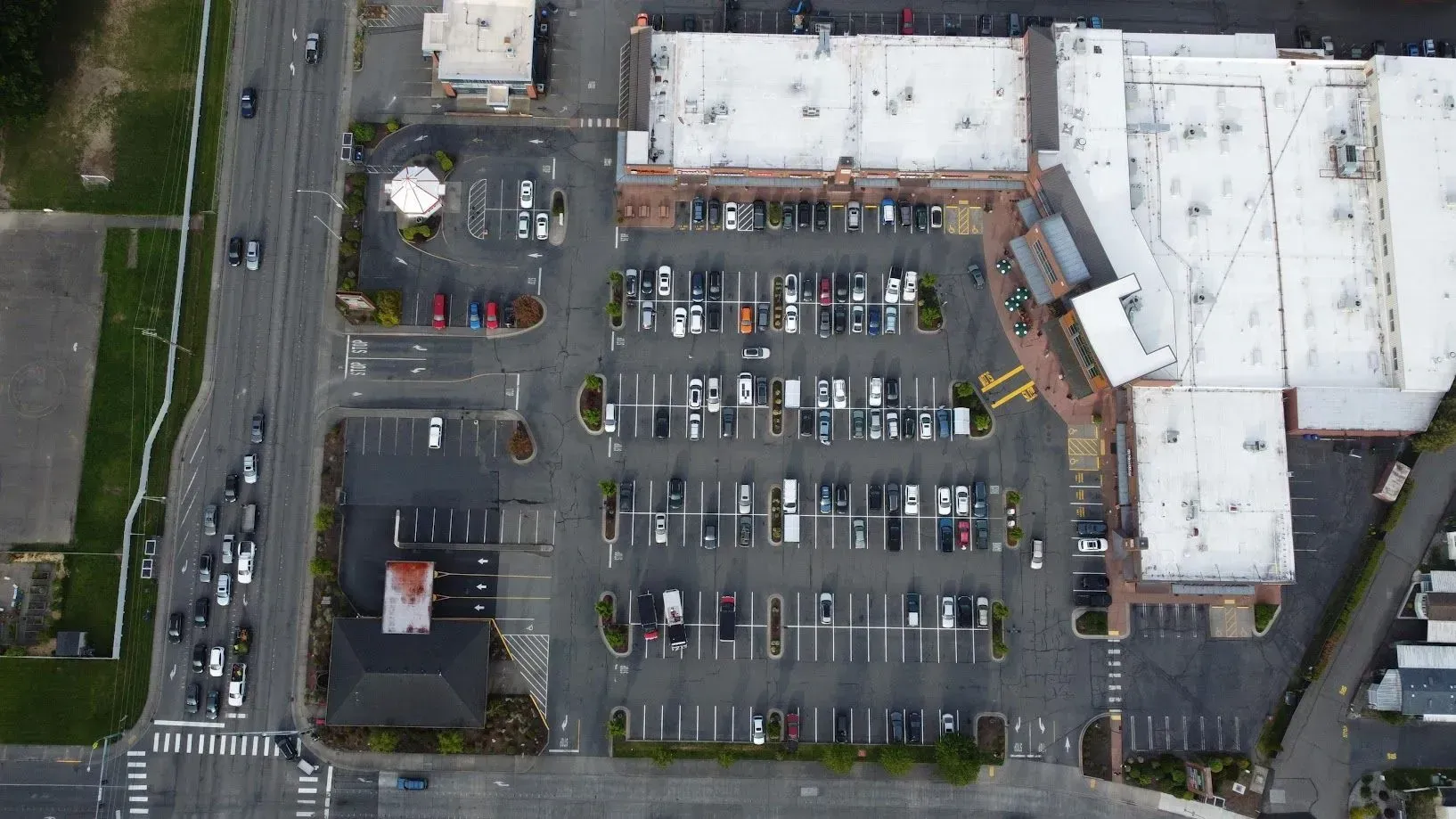 Aerial view of a parking lot and shopping center with many cars, near a road and buildings.