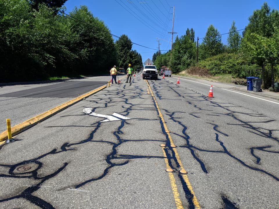Road repair: asphalt road with cracks being sealed; workers in vests.
