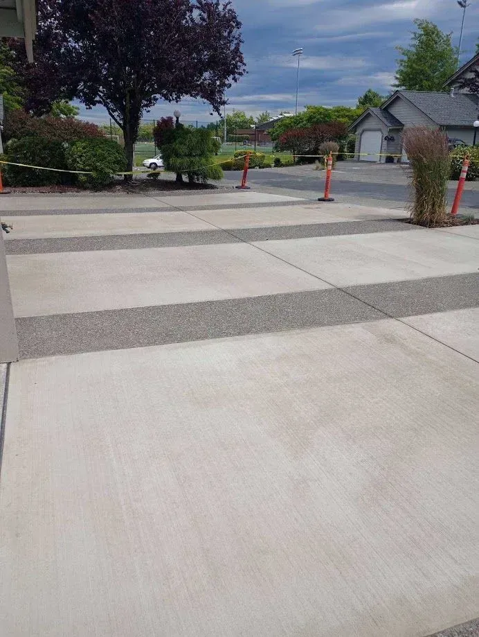 Concrete walkway with gravel inlays, orange safety posts, and a residential background.