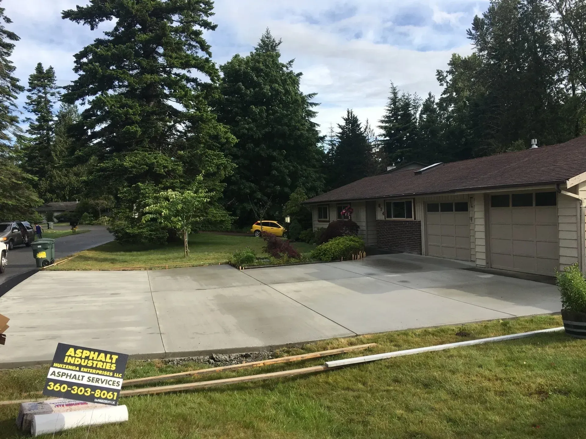 House with new concrete driveway; trees and green grass in the yard; asphalt services sign in foreground.
