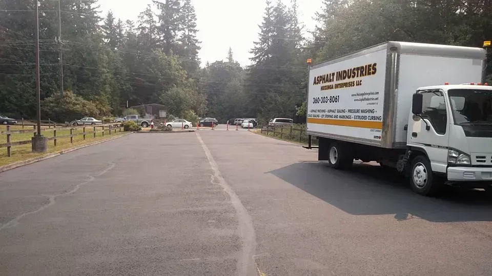 White moving truck parked on a paved road; trees and parked cars in background.