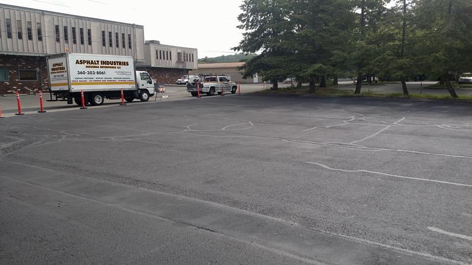 A parking lot with a delivery truck, car, and cones. Gray asphalt with faded parking space markings.