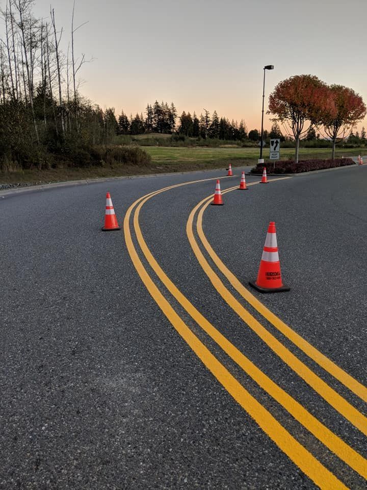 Orange traffic cones line a curving road with double yellow lines; a sunset backdrop.